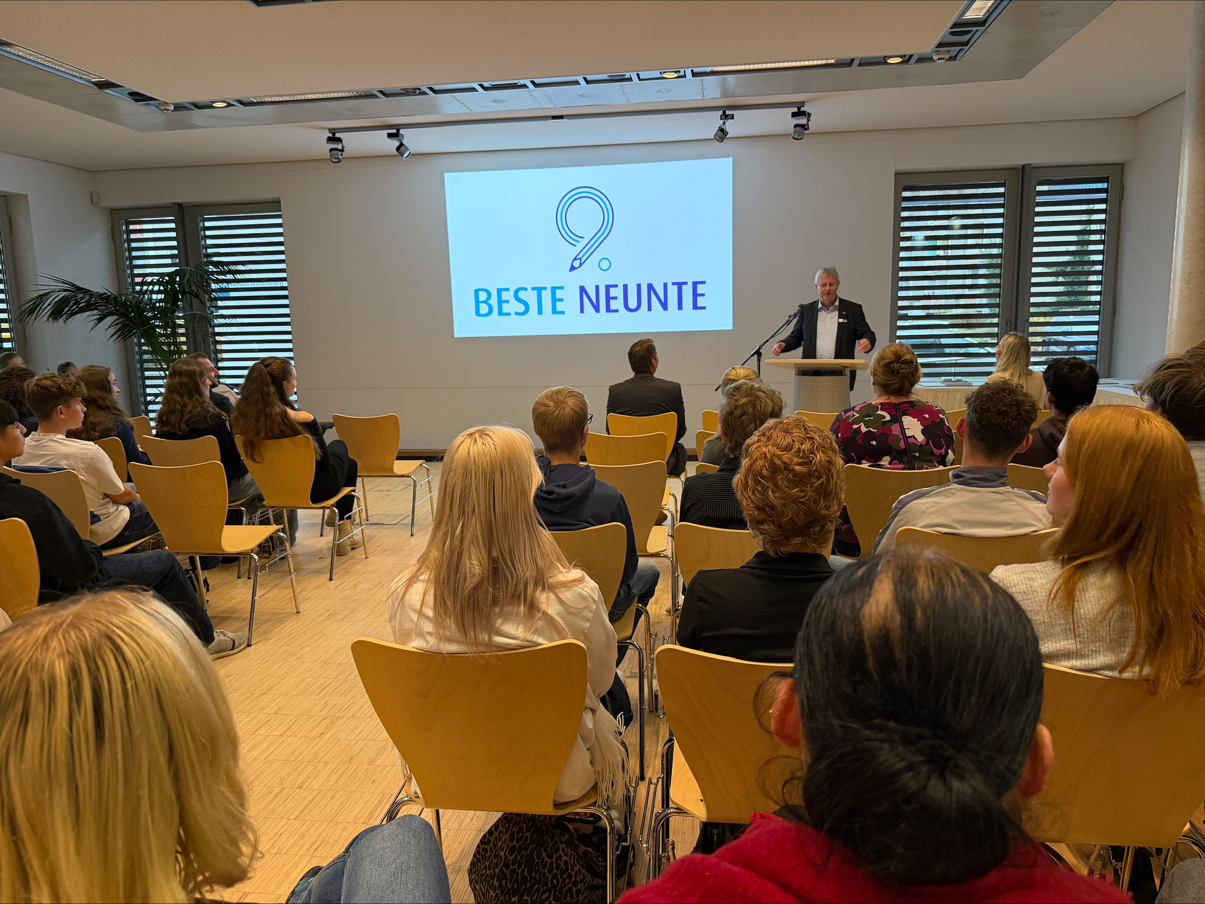 Torsten Haasch steht an einem Rednerpult und begrüßt das Publikum aus Schülerinnen und Schülern.