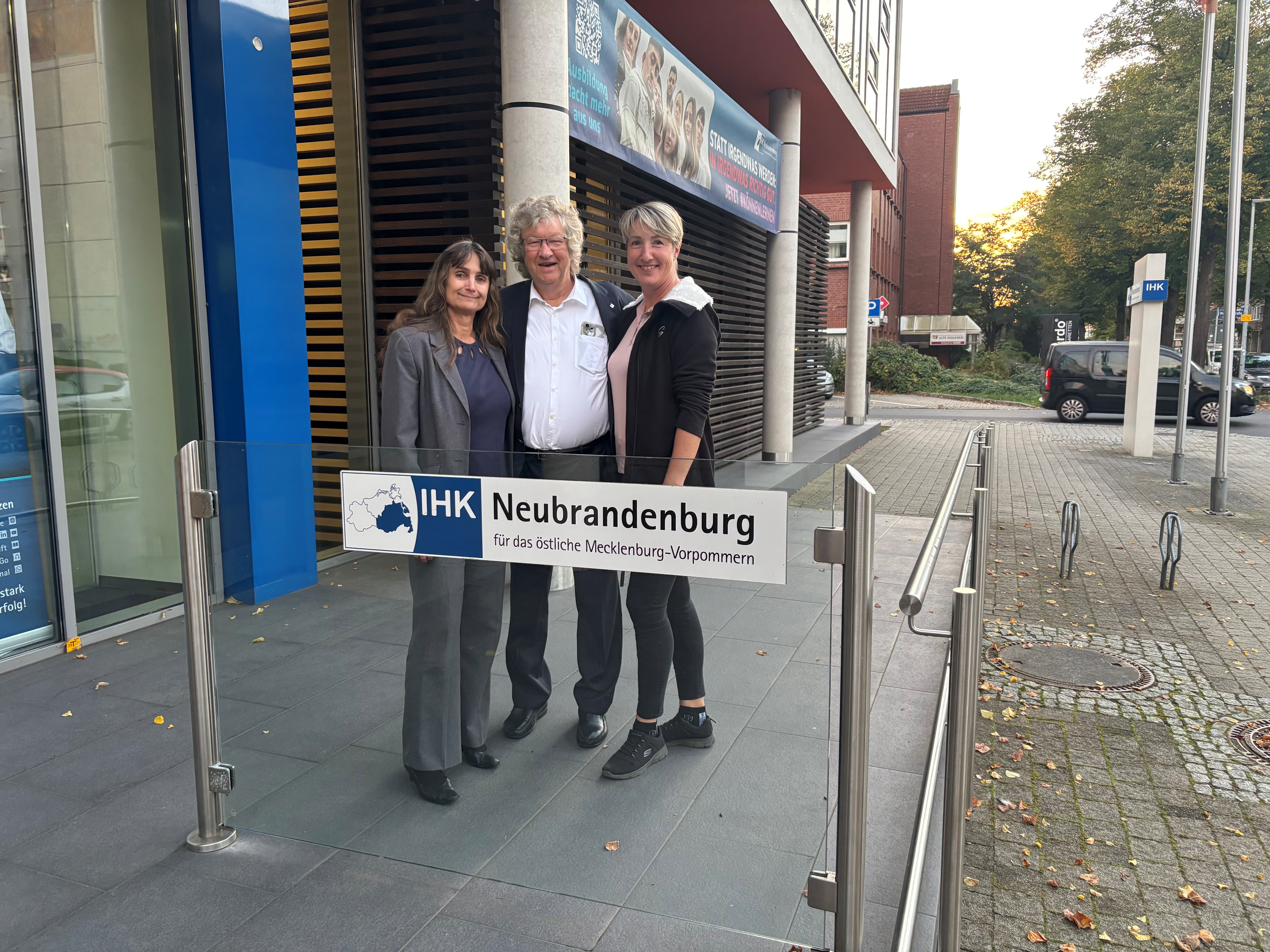 Drei Personen stehen für ein Foto hinter einem Schild der IHK.