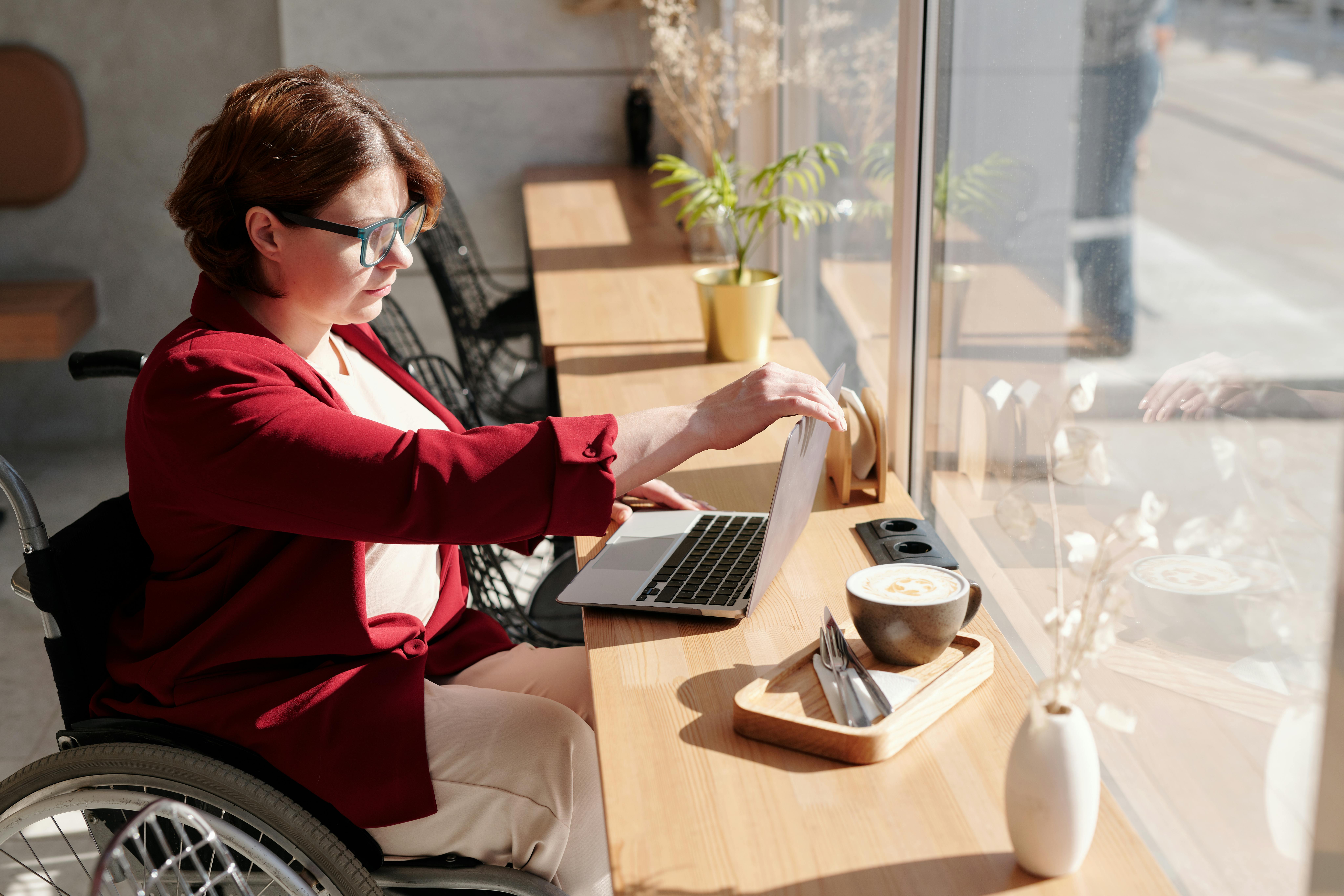 Eine Frau im Rollstuhl arbeitet an ihrem Laptop in einem Café..