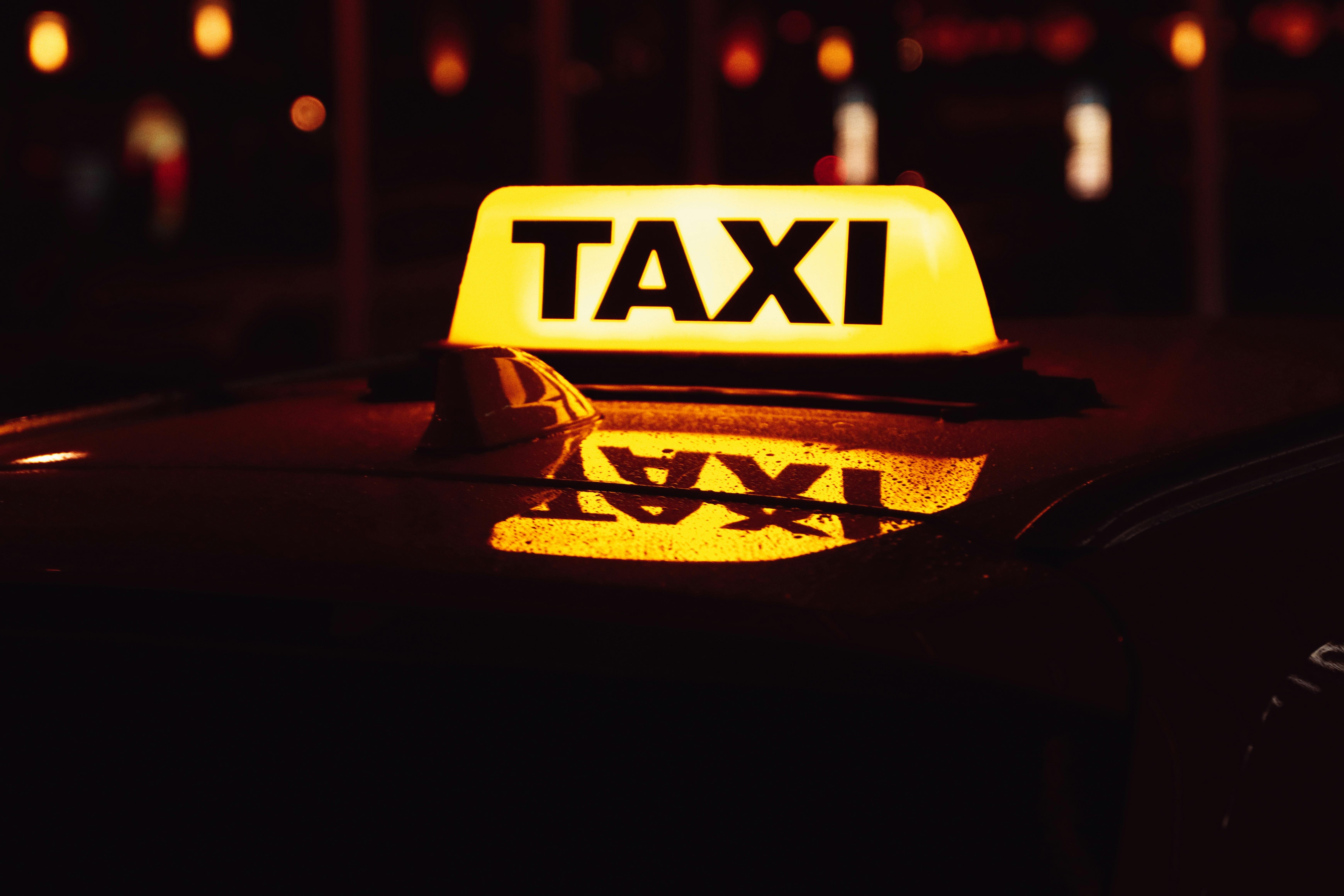 Ein beleuchtetes Taxischild bei Nacht.